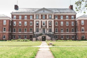 Home A historic brick building with classical elements, featuring a symmetrical facade and expansive lawn.
